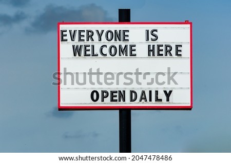 Retail open sign welcoming everyone during the Canadian pandemic restrictions, taken during the day against a light blue sky.