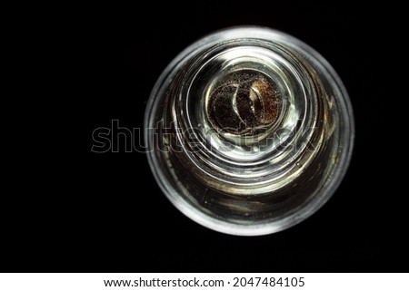 Wedding rings in a glass of champagne. Beverage gas bubbles around the jewelry. Isolate of glasses with champagne on a black background. Unique design elements for invitation, wedding cards.