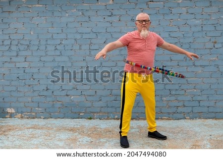 elderly man in yellow sweatpants spinning hoop on playground in front of house. Outdoor sports