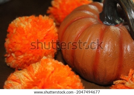 Closeup of decorative vivid orange Halloween pumpkin beside four brightly coloured orange and yellow pom poms against a background of brown and black.