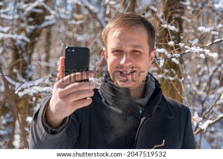 man in a coat takes a selfie in a snowy forest