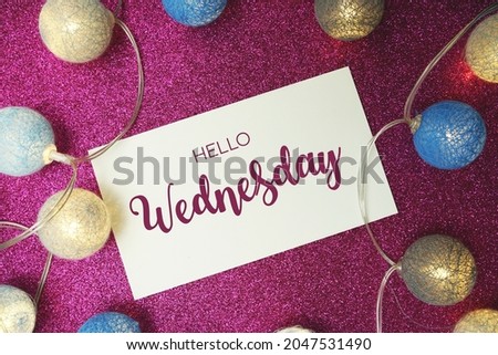 Hello Wednesday typography text with LED cotton ball on pink glitter background
