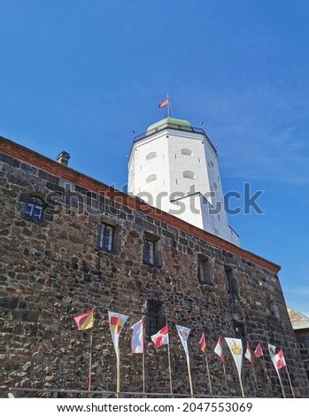Against the blue sky, the stone wall of Vyborg Castle, flags and the white Tower of St. Olaf in the city of Vyborg.