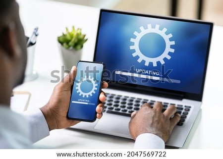 African American Man Doing Software Update On Mobile Phone And Laptop Royalty-Free Stock Photo #2047569722