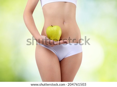 woman holding an apple with hands near the belly, on a green background