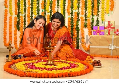 Mother and daughter in tradional clothes making rangoli at home on the occasion of deepawali festival with diya lamps ,flowers and mithai  Royalty-Free Stock Photo #2047626374