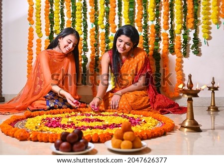 Mother and daughter in tradional clothes making rangoli at home on the occasion of deepawali festival with diya lamps ,flowers and mithai  Royalty-Free Stock Photo #2047626377