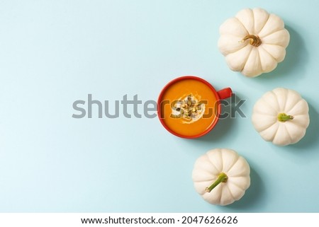Autumn pumpkins soup in orange plate with vegetables on blue background, modern concept, copy space