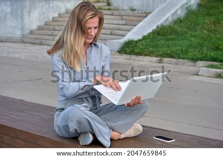 A woman with a laptop sits on a wooden platform, works online