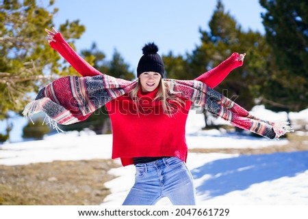 Young happy young blonde woman waving her scarf in the wind in a forest in the snowy mountains.