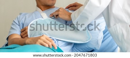 Woman doctor holding stethoscope checking male patient heartbeat vitals. Healthcare concept. Injured man has broken arm in cast lying on hospital bed. Female nurse visits painful man at accident ward. Royalty-Free Stock Photo #2047671803