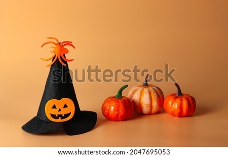 Front view of Halloween witch hat decorated with pumpkin head and spider with plastic pumpkins on orange background. Halloween costume party concept.