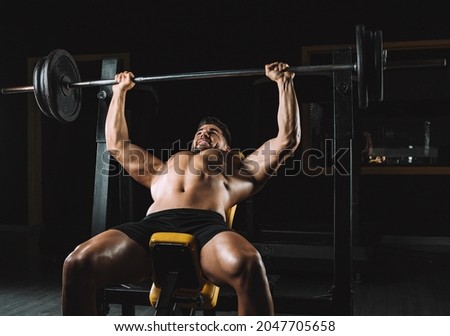 Adult caucasian male shirtless doing bench presses with weights in a bar in a dark gymnasium Royalty-Free Stock Photo #2047705658