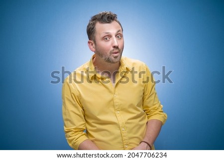 Distracted young man looking at other man over blue background, dresses in yellow shirt. Seducer man. Studio shot Royalty-Free Stock Photo #2047706234