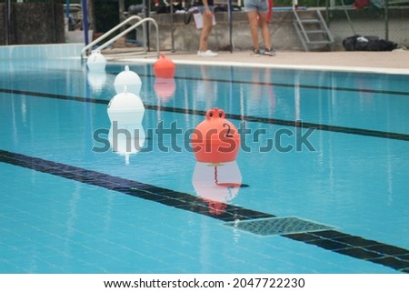 White and orange buoys in a calm swimming pool during a dog swimming race.