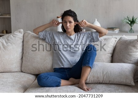 Full length unhappy young hispanic woman plugging fingers in ears, feeling stressed of noisy disturbing neighbors, refusing listening loud music, hating hearing sound of repairment works at home. Royalty-Free Stock Photo #2047731209