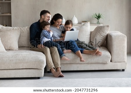 Happy affectionate loving hispanic family couple and small adorable children boy girl using computer, shopping in internet store, web surfing, watching cartoons online, resting on couch at home.