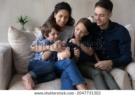 Caring young happy couple parents teaching small children son daughter saving money for future, planning own budget putting coins in small piggybank moneybox, financial literacy for kids concept. Royalty-Free Stock Photo #2047731302