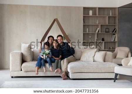 Full length joyful young married hispanic couple parents sitting with little children son daughter on comfortable couch under carton roof, celebrating moving into own dwelling, real estate concept. Royalty-Free Stock Photo #2047731356