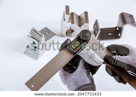 Worker measures the angle of deflection of metal parts on a white background with a protractor.