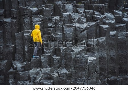 Man wearing yellow coat looking up at Reynisdrangar basalt columns at Reynisfjara Beach, Iceland Royalty-Free Stock Photo #2047756046