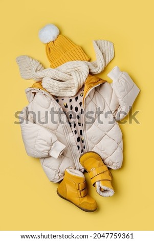Kids warm puffer jacket with hat and boots on yellow  background. Stylish childrens outerwear. Winter fashion outfit  Royalty-Free Stock Photo #2047759361