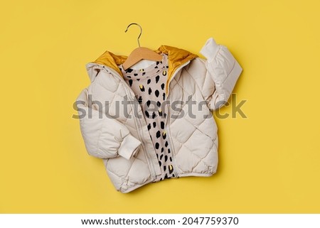 Kids warm puffer jacket hanging on a hanger on yellow  background. Stylish childrens outerwear. Winter fashion outfit  Royalty-Free Stock Photo #2047759370