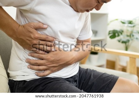 Asian male patient with abdominal pain on right side belly,painful in abdomen,irritable bowel,middle-aged man holds under the ribs,stomach ache,cirrhosis of the liver disease,liver cancer concept Royalty-Free Stock Photo #2047761938