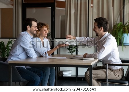 Realtor giving key from first home to happy family couple of clients. Married customers meeting with real estate agent, house seller, landlord in office for property buying or rent deal