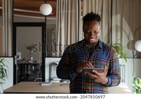 Happy millennial self employed professional using tablet in office. Young African American hipster guy, student, employee using virtual app, online service on pad computer, chatting, browsing Royalty-Free Stock Photo #2047810697