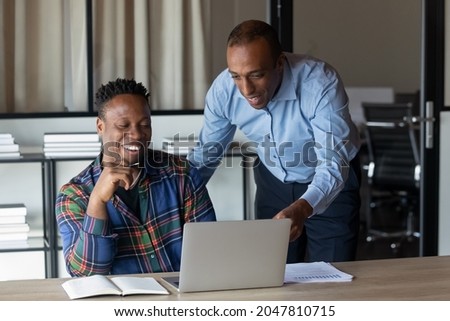 Happy African American employees watching and discussing video presentation on laptop, working on project together, looking at screen, smiling. Middle aged mentor supervising intern work. Teamwork Royalty-Free Stock Photo #2047810715