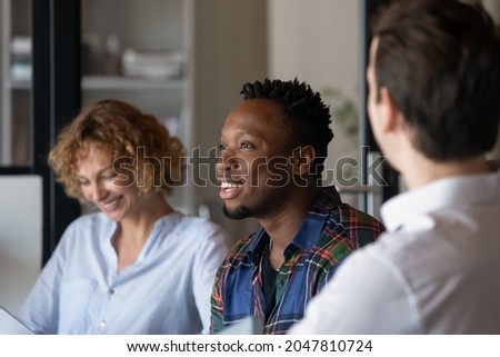 Diverse team of office employees discussing project together, brainstorming, talking, laughing. Smiling African American guy visiting group therapy meeting, sharing funny story to laughing groupmates Royalty-Free Stock Photo #2047810724