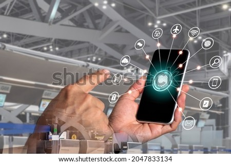 A man's hand holding a phone with the symbol for utilizing internet applications, booking lodging, booking flights, and shopping on computers on his right-hand screen, which is lighted in blue.
