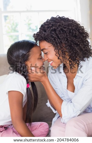 Pretty mother sitting on couch with cute daughter at home in the living room