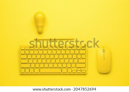 A yellow keyboard with a mouse, a pencil and a light bulb on a yellow background. The concept of business and minimalism. Monochrome. Royalty-Free Stock Photo #2047852694