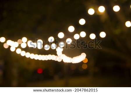 Blurred abstract background, backyard illumination, light in the evening garden, electric Defocused garland. Lamp garland of light bulbs on trees illuminate night scene Royalty-Free Stock Photo #2047862015