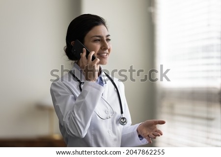 Happy Indian doctor giving telephone consultation, talking to patient on mobile phone, making call from hospital office. General practitioner, therapist, counselor answering questions on hotline Royalty-Free Stock Photo #2047862255