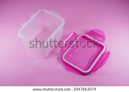Small transparent plastic container for storing food. Airtight container with rubber seal. Container with pink lid on pink background isolated. Royalty-Free Stock Photo #2047863074