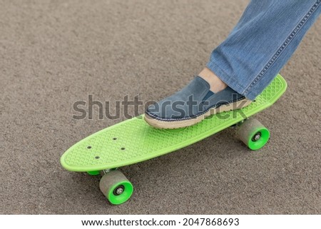 men's legs in blue moccasins on a children's green skateboard