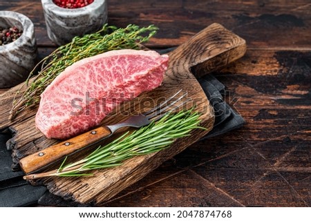 Wagyu A5 raw rump or sirloin steak, kobe beef meat on a butchery board. Dark wooden background. Top view. Copy space