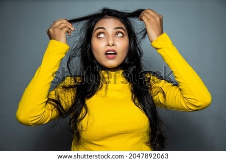 Beautiful Frustrated Indian Young Woman With Long Disheveled Hair.
Holding Messy Un-brushed Dry black Hair In Hands. Hair Damage, Health And Beauty Concept.
 Royalty-Free Stock Photo #2047892063
