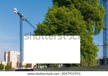 Blank white billboard for advertisement in front of the construction site. Apartment building under construction on a sunny day.