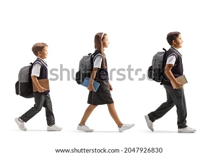 Full length profile shot of a schoolgirl and two schoolboys walking in line with books in their hands isolated on white background