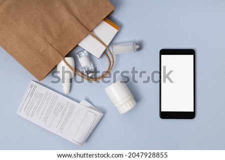 Top view of empty screen of smartphone, paper bag full of bottles of pills,bill for payment on the blue desk.Online medicine order Royalty-Free Stock Photo #2047928855