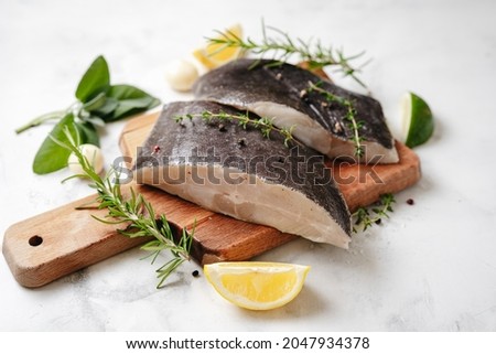 Top view of two raw halibut fish steaks with herbs and lemon on wooden board and white background. Omega 3 fats good for mental clarity. Brain food