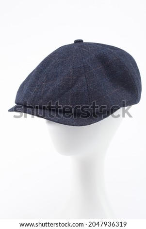 A dark blue checkered peaked cap with a visor on the head of a white mannequin. Blue checkered peaked cap isolated over white background.