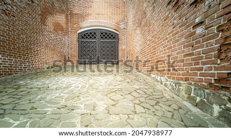 Decor and architectural elements. Antique carved wooden black gate of the old castle in the red brick wall. Horizontal photo.