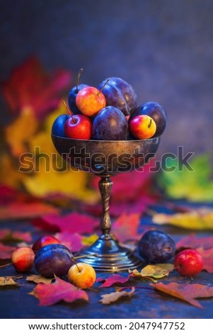 Plum blue and small apples in a vase with autumn leaves.