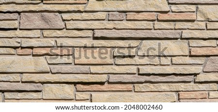 Sandstone building wall constructed in multi-colored, different sized stones in a pleasing horizontal pattern.