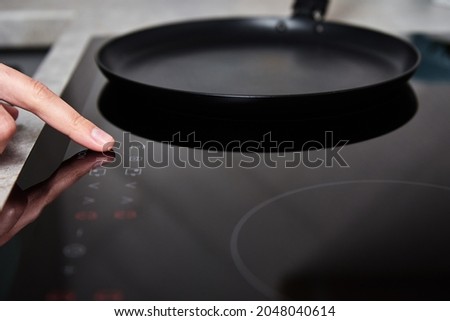 Modern kitchen appliance. Woman hand turn on induction stove to cook. Finger touching sensor button on induction or electrical hob Royalty-Free Stock Photo #2048040614
